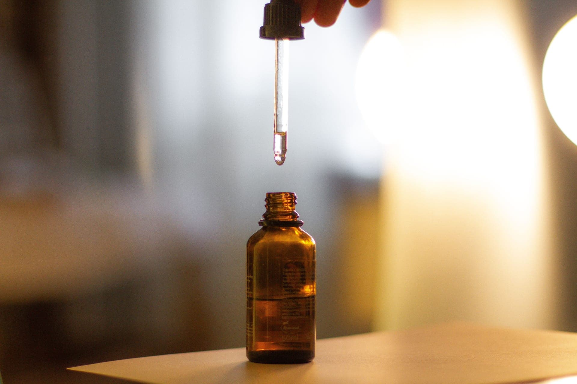 An amber glass serum dropper on a warm, dark surface in low evening light